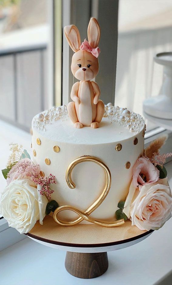 a white cake with gold decorations and a rabbit on top