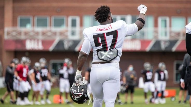 a football player is walking on the field with his hands in the air and other players behind him