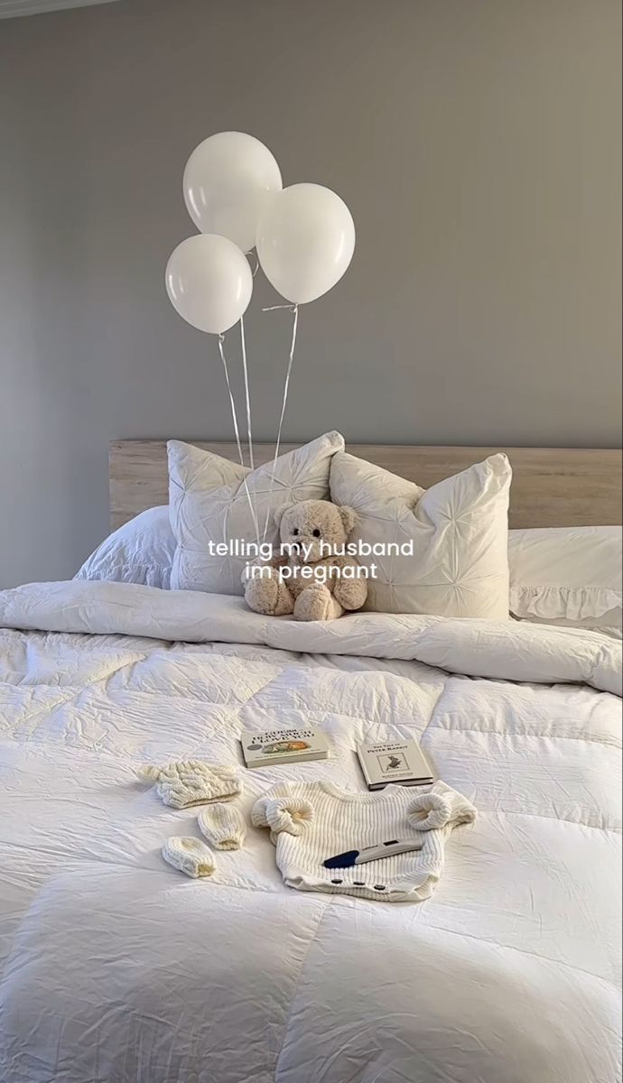 a teddy bear sitting on top of a bed next to three white balloons in the air