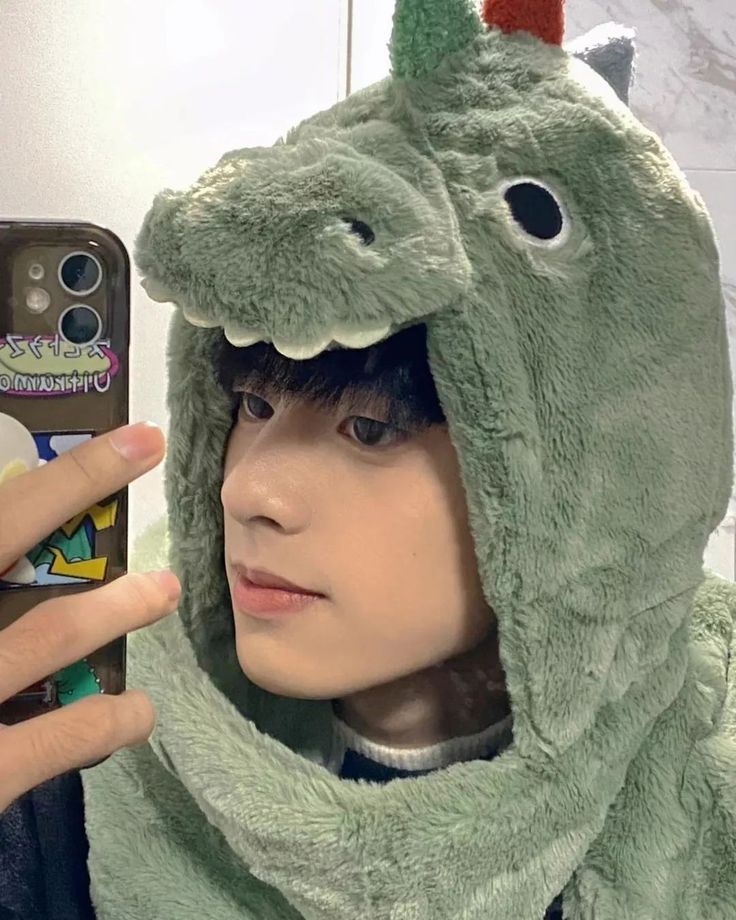 a person in a dinosaur costume taking a selfie with a cell phone while wearing a hoodie