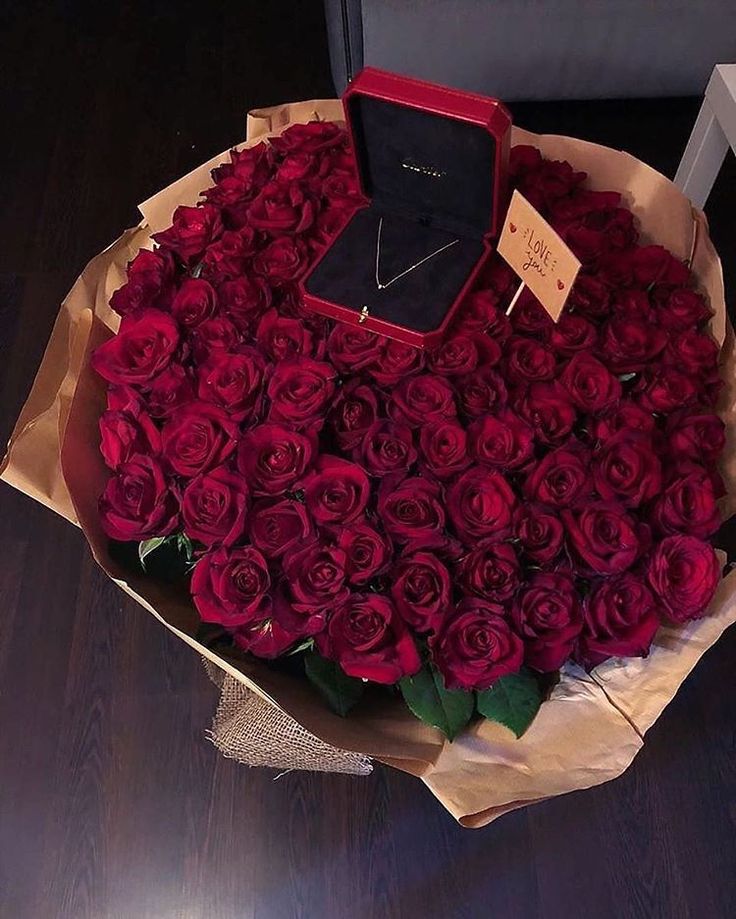 a large bouquet of red roses in a box with a necklace on it's neck