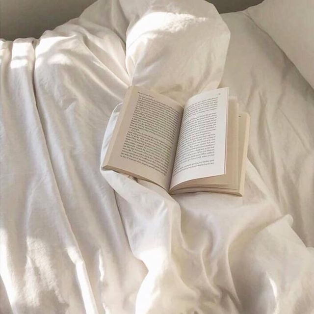 an open book laying on top of a white bed with sheets and pillows in front of it