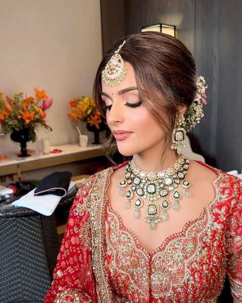 a woman wearing a red and gold bridal outfit with jewelry on her head, sitting in front of a desk