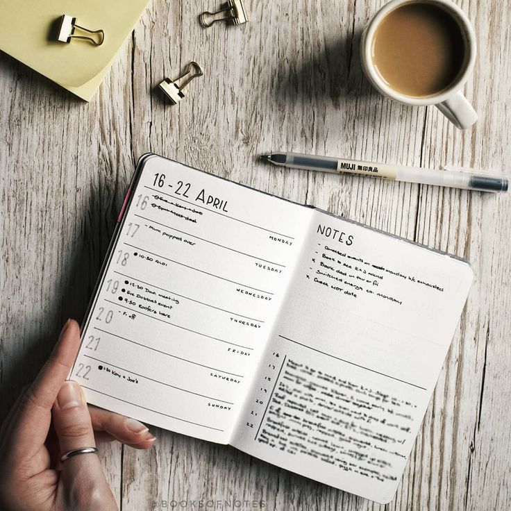 a person is holding an open book on a wooden table with office supplies and coffee