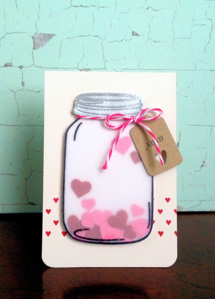 a handmade card with a mason jar and hearts on the front, hanging from a wooden table