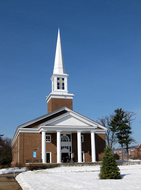 a church with a steeple and white columns in the snow on a sunny day