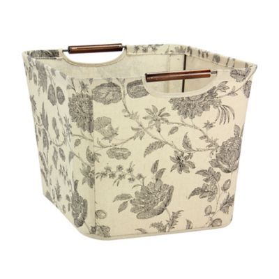 a fabric storage bin with handles and flowers on the front, one side has a wooden handle