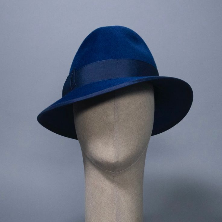 A timeless fedora inspired by the sultry style of Marlene Dietrich. In rich lapis blue velour felt with grosgrain band and bow. Materials: Ethically sourced fur felt, Grosgrain Ribbon, Millinery Wire Style: Fedora Measurements: Crown height 4.25 in (11 cm) Brim width at deepest over right eye 3.25 in (6 cm) Hat Box: 14 in How to Wear: Classic fit Ready to Ship in a size L (23 in / 58 cm). Other sizes will be Made to Order. Katrina is part of the A/W 2023 "Stardust and Stories" collection. Limite Luxury Fitted Fedora For Kentucky Derby, Luxury Fur Felt Fedora For Kentucky Derby, Blue Fedora With Short Brim For Parties, Classic Short Brim Fedora For Evening, Classic Evening Fedora With Short Brim, Evening Fur Felt Fedora Hat, Luxury Curved Brim Felt Hat For Formal Occasions, Classic Fitted Fedora For Evening, Fitted Classic Evening Fedora