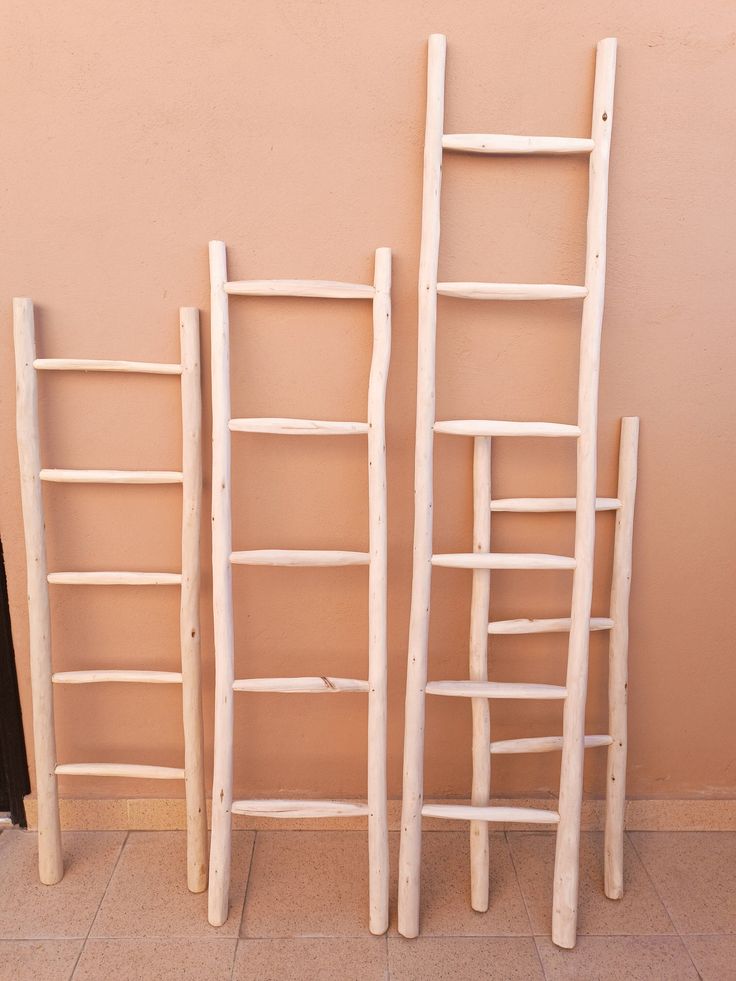 three wooden ladders sitting next to each other on top of a tile floor in front of a pink wall