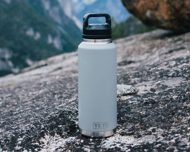 a stainless steel water bottle sitting on top of a rocky cliff overlooking the valley below