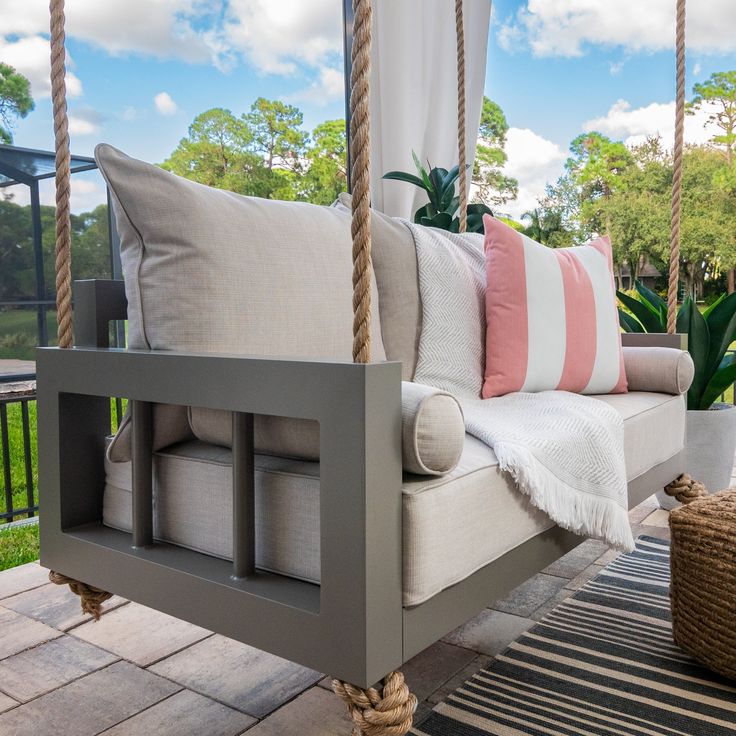 a porch swing with cushions and pillows on the back patio, next to a potted plant