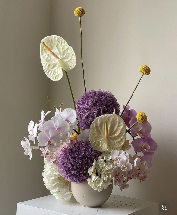 a white vase filled with lots of purple and white flowers on top of a table