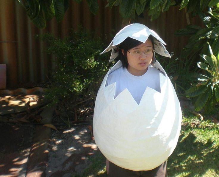 a woman dressed in an egg costume standing next to a tree and bushes with her hands on her hips