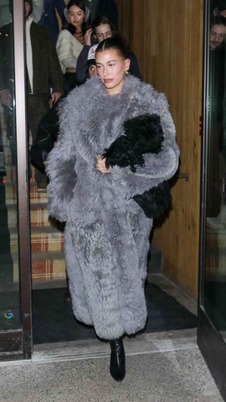 a woman is walking out of an elevator wearing a fur coat