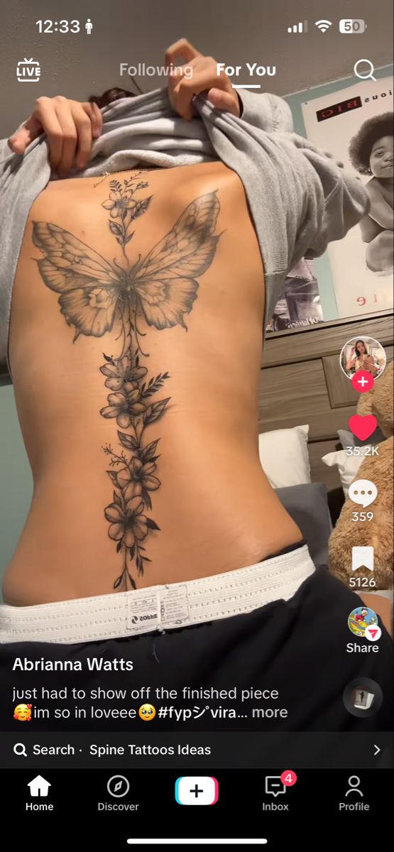 the back of a woman's stomach with a butterfly and flowers tattoo on it