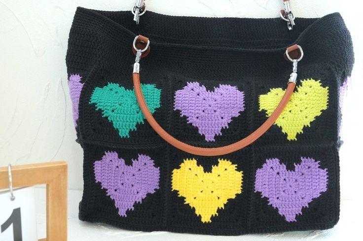 a crocheted handbag with hearts on it hanging from a hook in front of a white wall