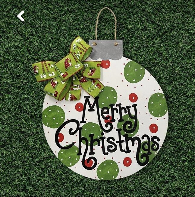 a christmas ornament hanging on the grass with a green bow and merry christmas message