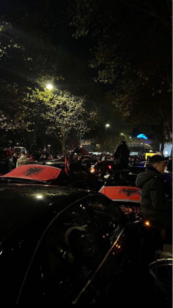 a group of people standing around parked cars at night