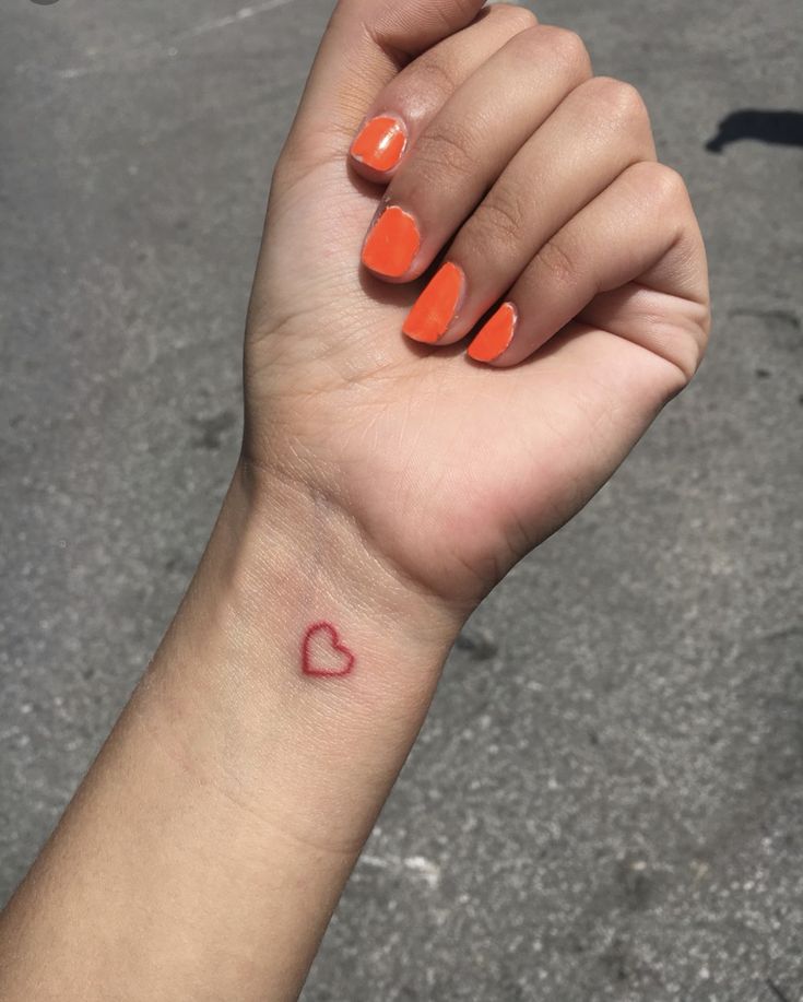 a woman's hand with an orange and red heart tattoo on her left wrist