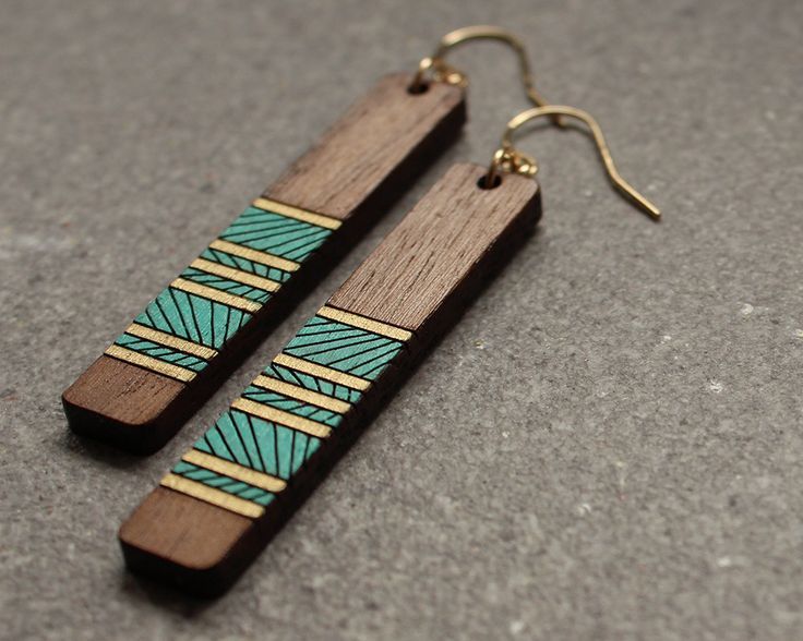 two wooden earrings with blue and green designs on them sitting on a gray surface in front of a pair of gold - plated ear wires