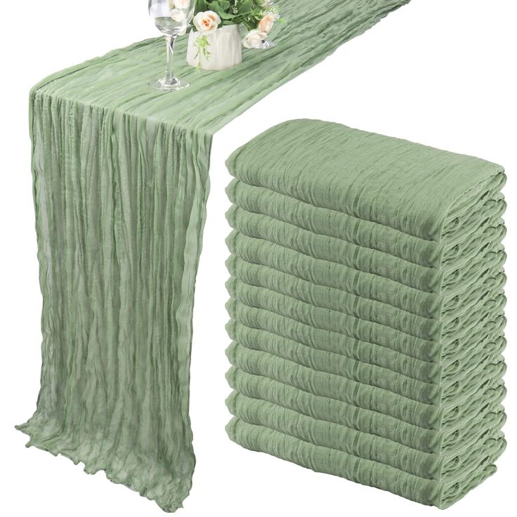 a stack of green cloths next to a vase with flowers and wine glasses on it