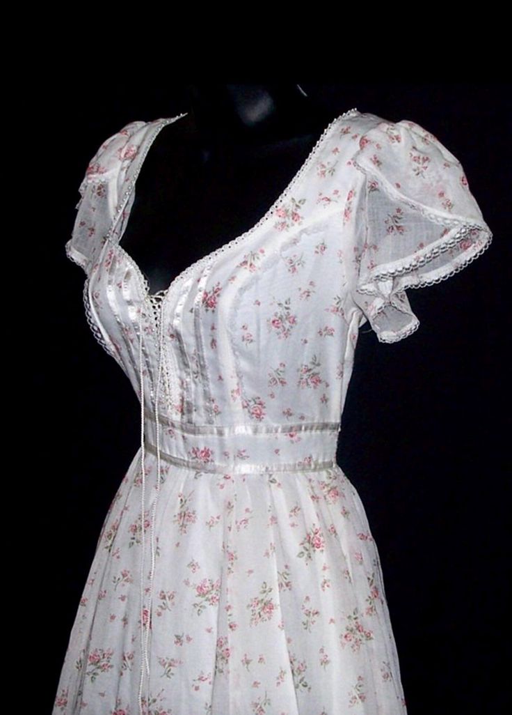 This is a vintage Gunne Sax dress from the 70s. It's made from a cotton blend material with pink roses and a white background. Its trimmed with lace, ribbon, and pearls. The inside is lined. The front laces up like a corset. The corset can be loosened slightly to add a little more room if needed. The bottom has a full skirt with an attached slip underneath. It zips and ties in the back. CONDITION: Great condition, no flaws found. New with tag. ESTIMATED SIZE: XS. The size tag is marked as a 7 in Gunne Sax Prom Dress, Fitted Victorian Cotton Dresses, Fitted Cottagecore Dress For Vintage Occasions, Cottagecore Fitted Dress In Vintage Style, Fitted Cottagecore Dresses For Vintage Events, Fitted Cotton Vintage Dress For Garden Party, Fitted Victorian Vintage Dress For Garden Party, Feminine Vintage White Dress, Cottagecore Fitted Vintage Dress With Empire Waist