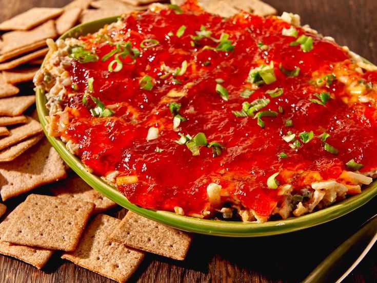 a green bowl filled with pizza dip surrounded by crackers