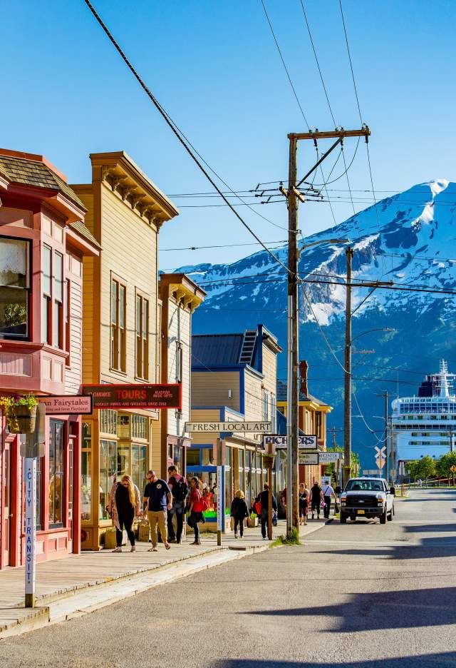 people are walking down the street in front of some buildings with mountains in the background