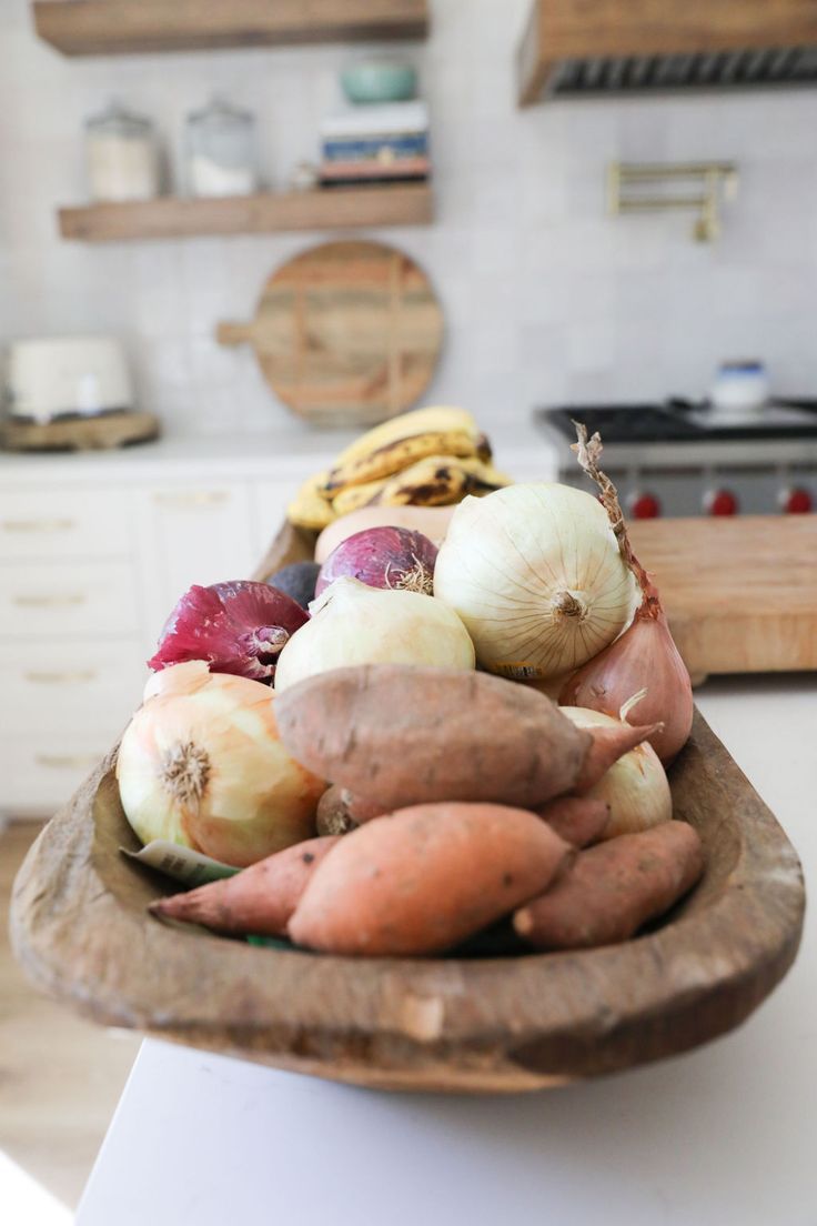 a wooden bowl filled with vegetables on top of a counter next to a stovetop