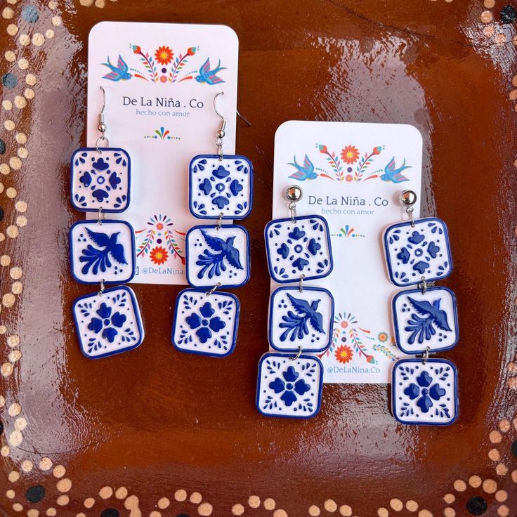 blue and white tile earrings are displayed on a brown surface with polka dots around them