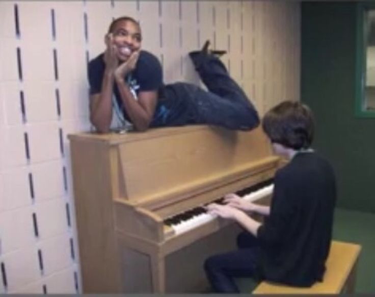 two young men sitting at a piano in a room with white tiles on the walls