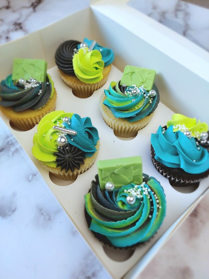 cupcakes with green, blue and black frosting in a box