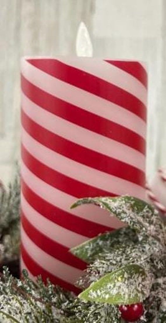 a red and white striped candle sitting on top of a christmas wreath next to greenery