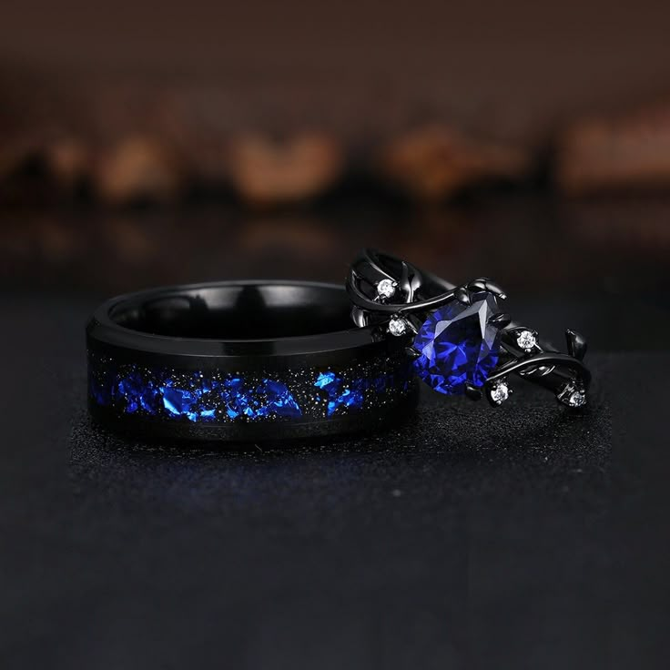 two wedding bands with blue and black diamonds on them, sitting next to each other