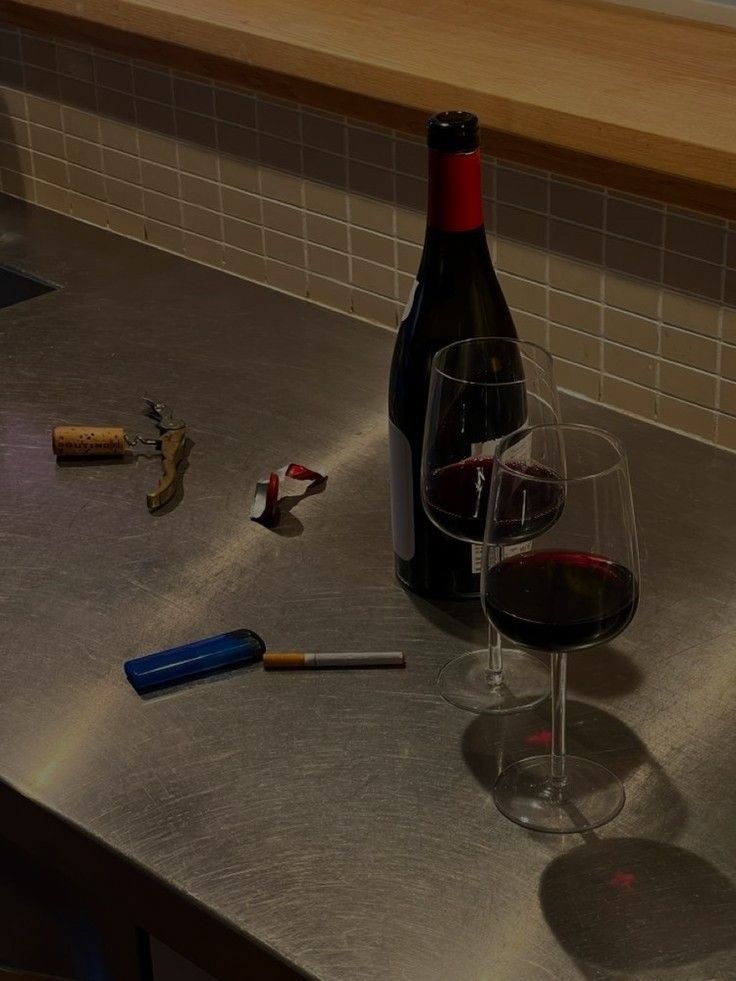 a bottle of wine sitting on top of a counter next to a glass filled with red wine