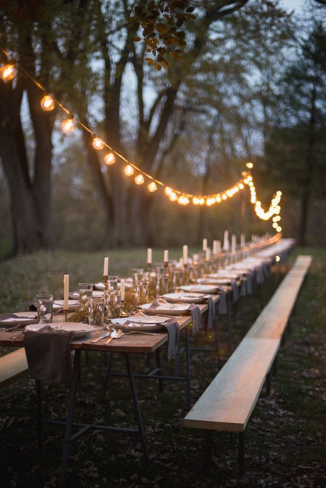 a long table is set with candles and place settings for an outdoor dinner in the woods