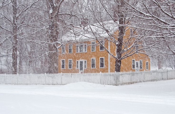 a yellow house in the middle of winter with snow on the ground and trees around it