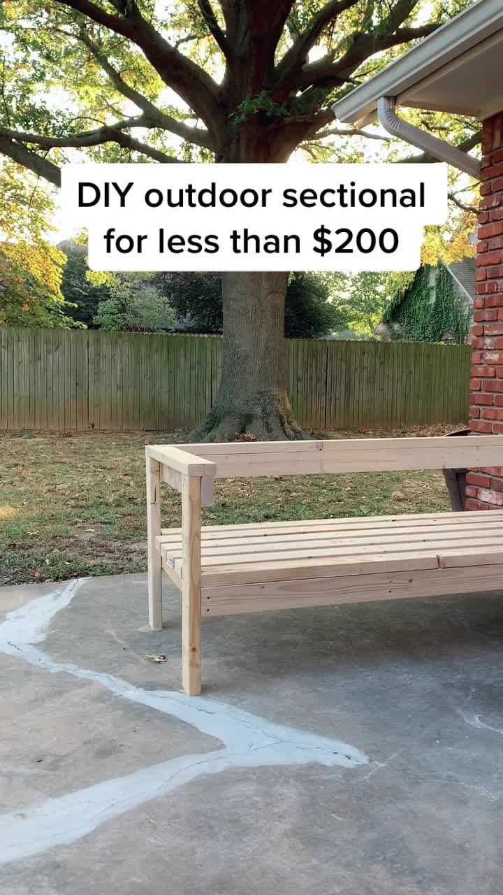 a wooden bench sitting in front of a tree on the side of a building with text overlay that reads diy outdoor sectional for less than $ 20