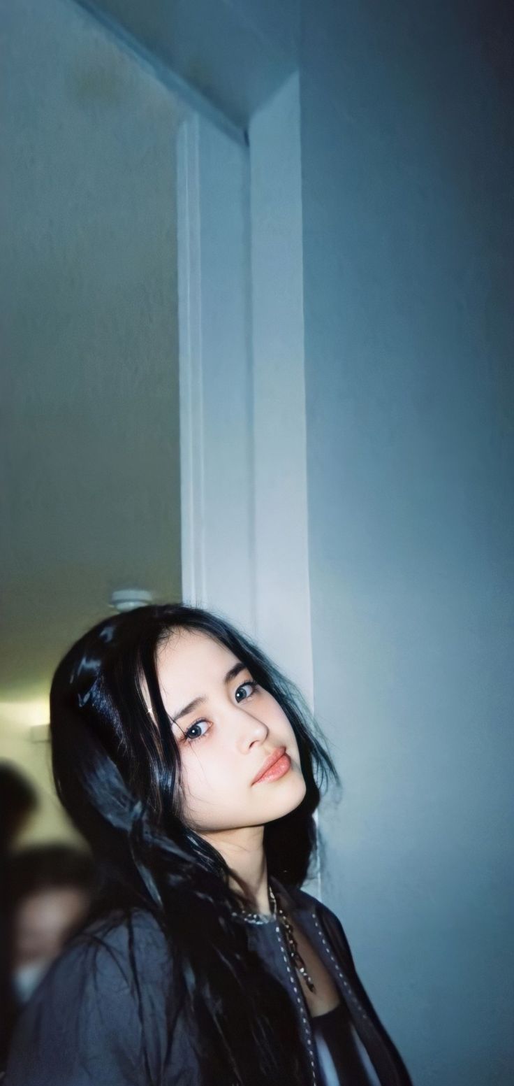 a woman with long black hair standing in front of a door and looking off into the distance