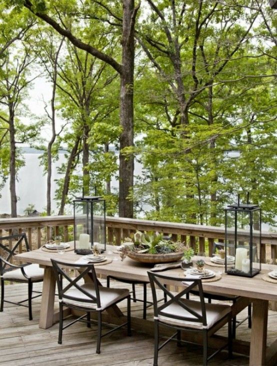 an outdoor dining table and chairs on a wooden deck with trees in the back ground