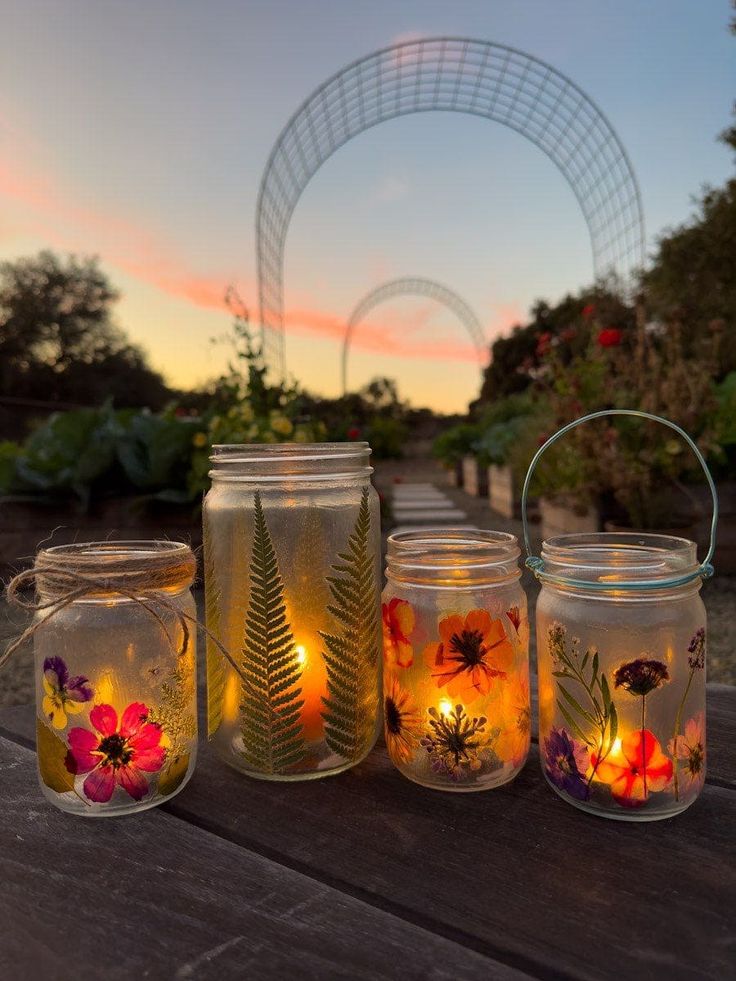 four mason jars filled with flowers and lit candles