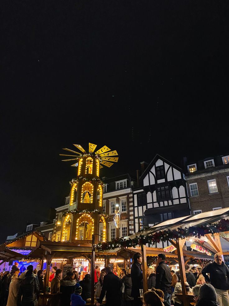 people are standing in front of an outdoor market with lights and decorations on the buildings