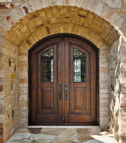 an arched wooden door with two sidelights and brick walls in front of a stone building