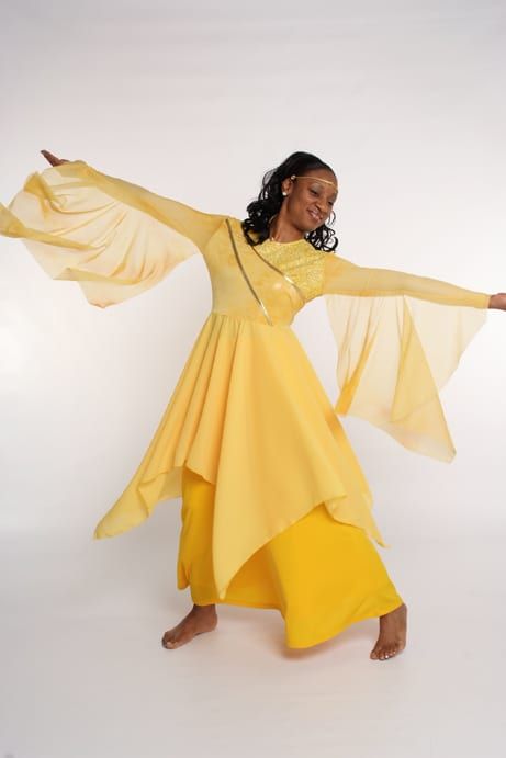 a woman in yellow is dancing with her arms outstretched