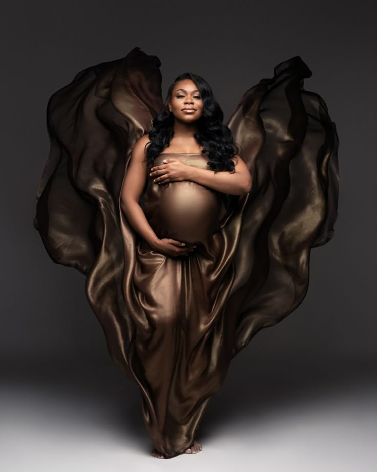 a pregnant woman in a flowing dress with her hands on her belly, posing for the camera