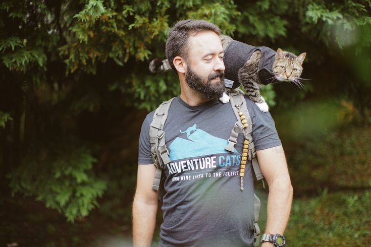 a man with a cat on his back walking in the woods while wearing a backpack