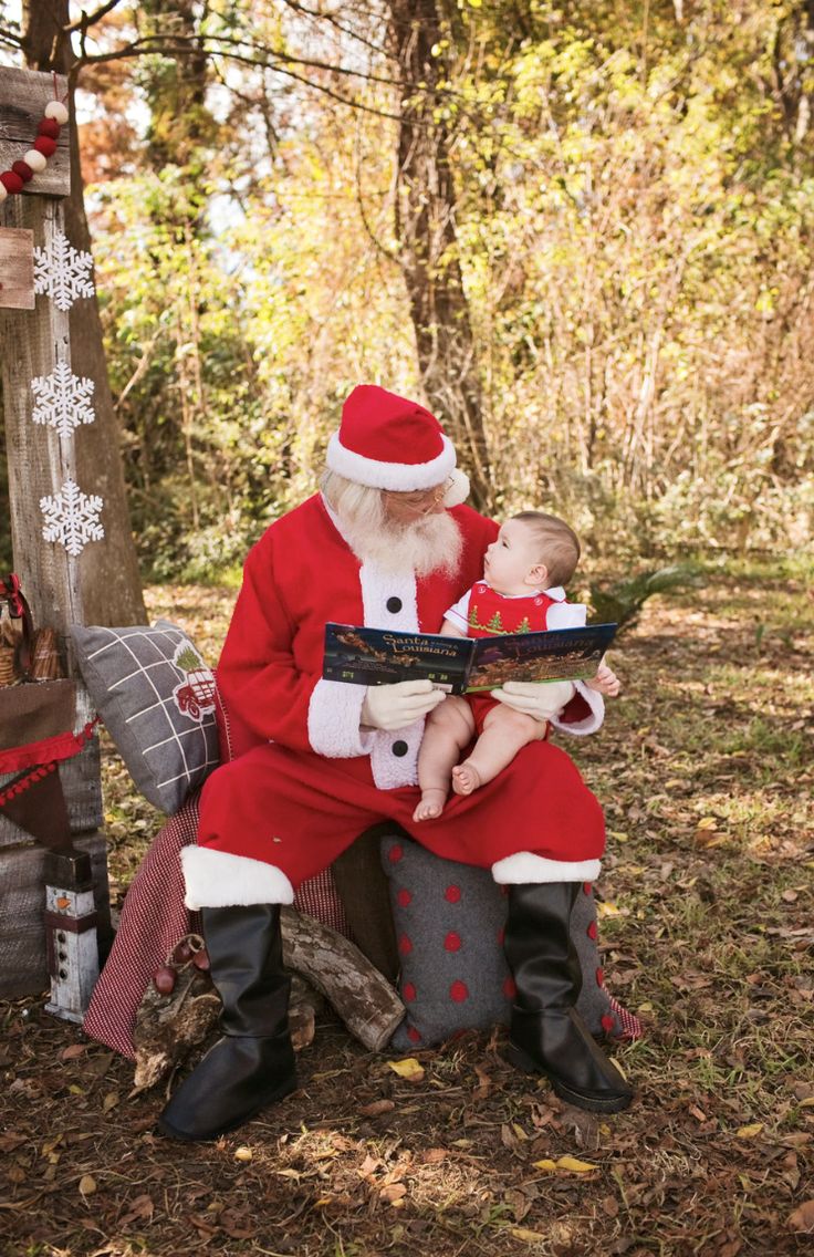 a man dressed as santa claus sitting on a bench holding a baby in his lap