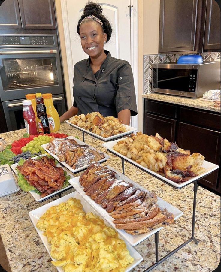 a woman standing in front of several trays of food on top of a kitchen counter