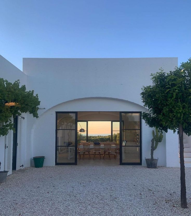 the entrance to a house with two trees in front of it and an open patio area