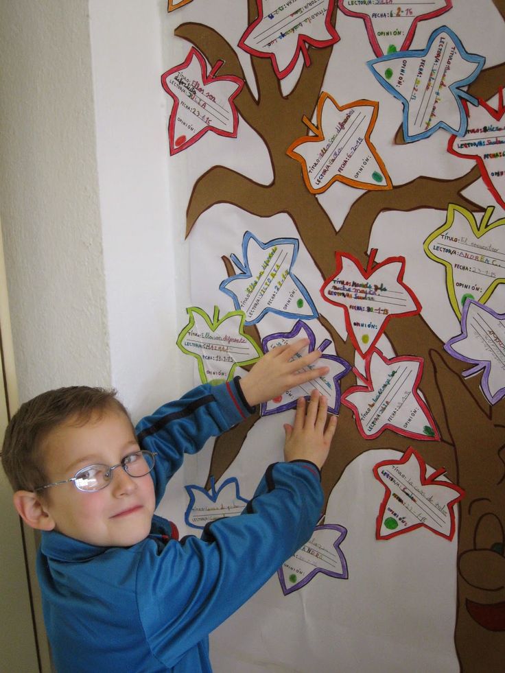 a young boy writing on a bulletin board next to a tree with leaves and branches